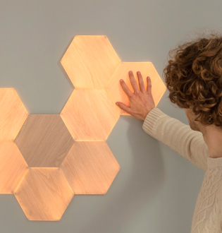壁に取り付けたNanoleaf Elements Wood Look Hexagonsの画像です。 スマートライトパネルはタッチと音楽に反応し、優しい光でおうちを満たします。 木製風デザインパネルにタッチし、大好きな曲をプレイして、レイアウトにダイナミックな光を解き放とう。