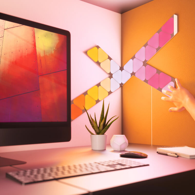 Nanoleaf Shapes Thread-enabled color-changing mini triangle smart modular light panels mounted to a wall above a desk. Similar to Philips Hue, Lifx. HomeKit, Google Assistant, Amazon Alexa, IFTTT. 